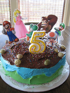 Birthday cake with number 5 candle and paper Mario brothers toppers.