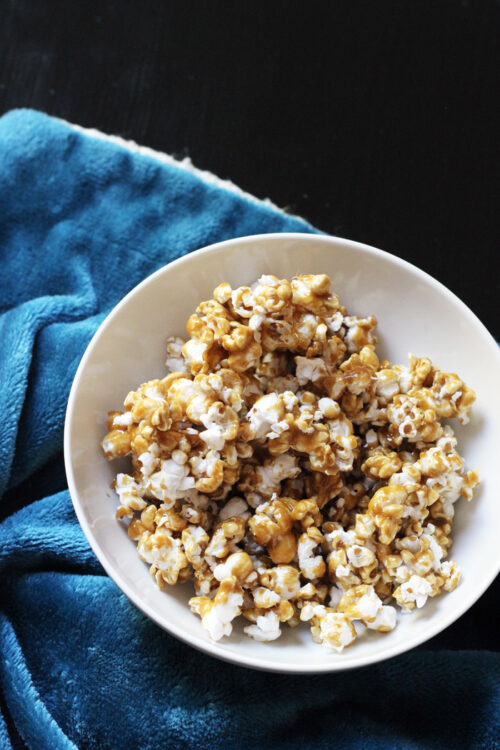 A bowl of Caramel Popcorn atop a blue plush blanket.