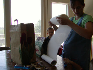 A person standing next to a window, with paper towels to make homemade pinata.