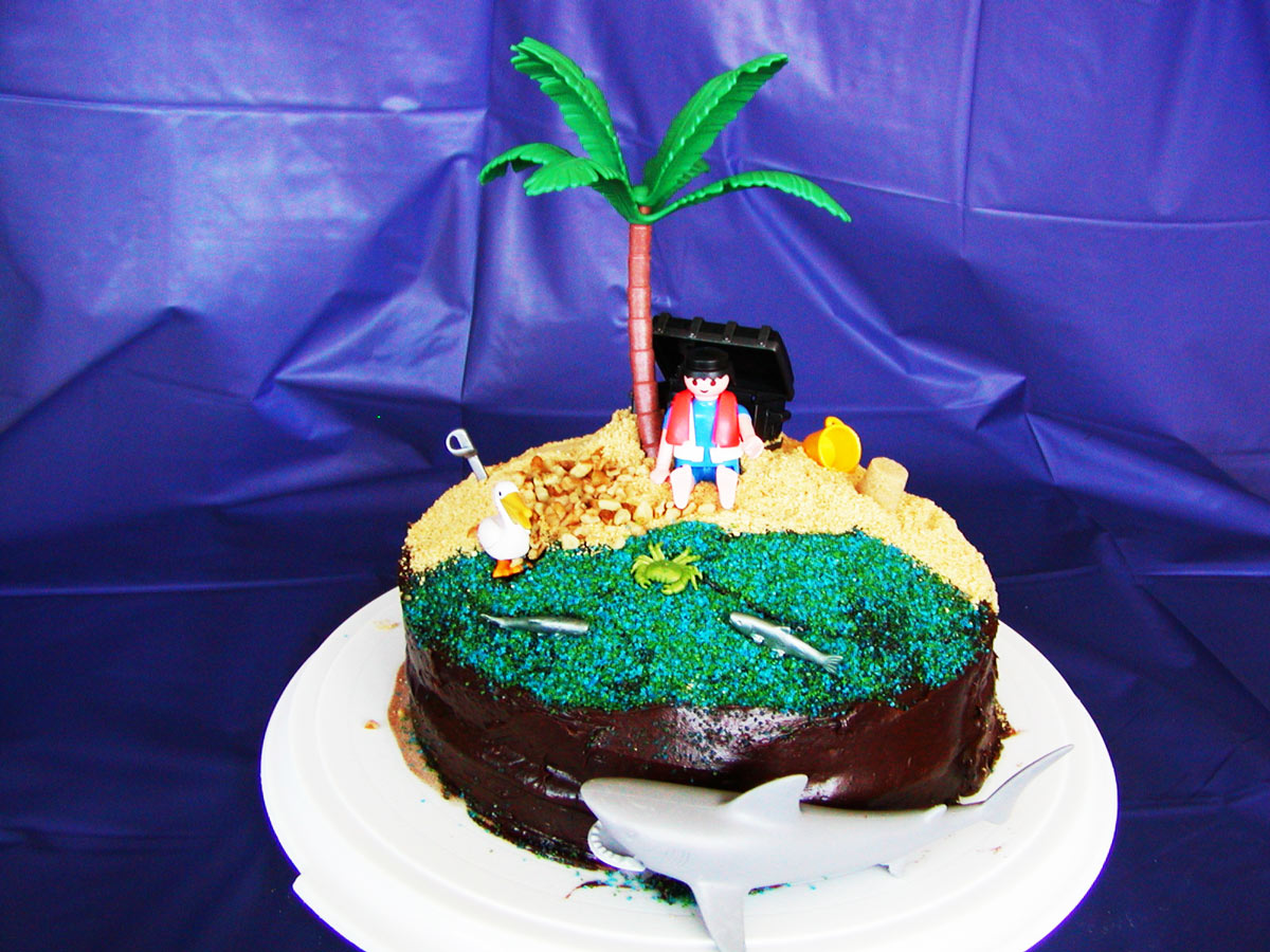 chocolate layer cake decorated like a beach with palm tree and shark.
