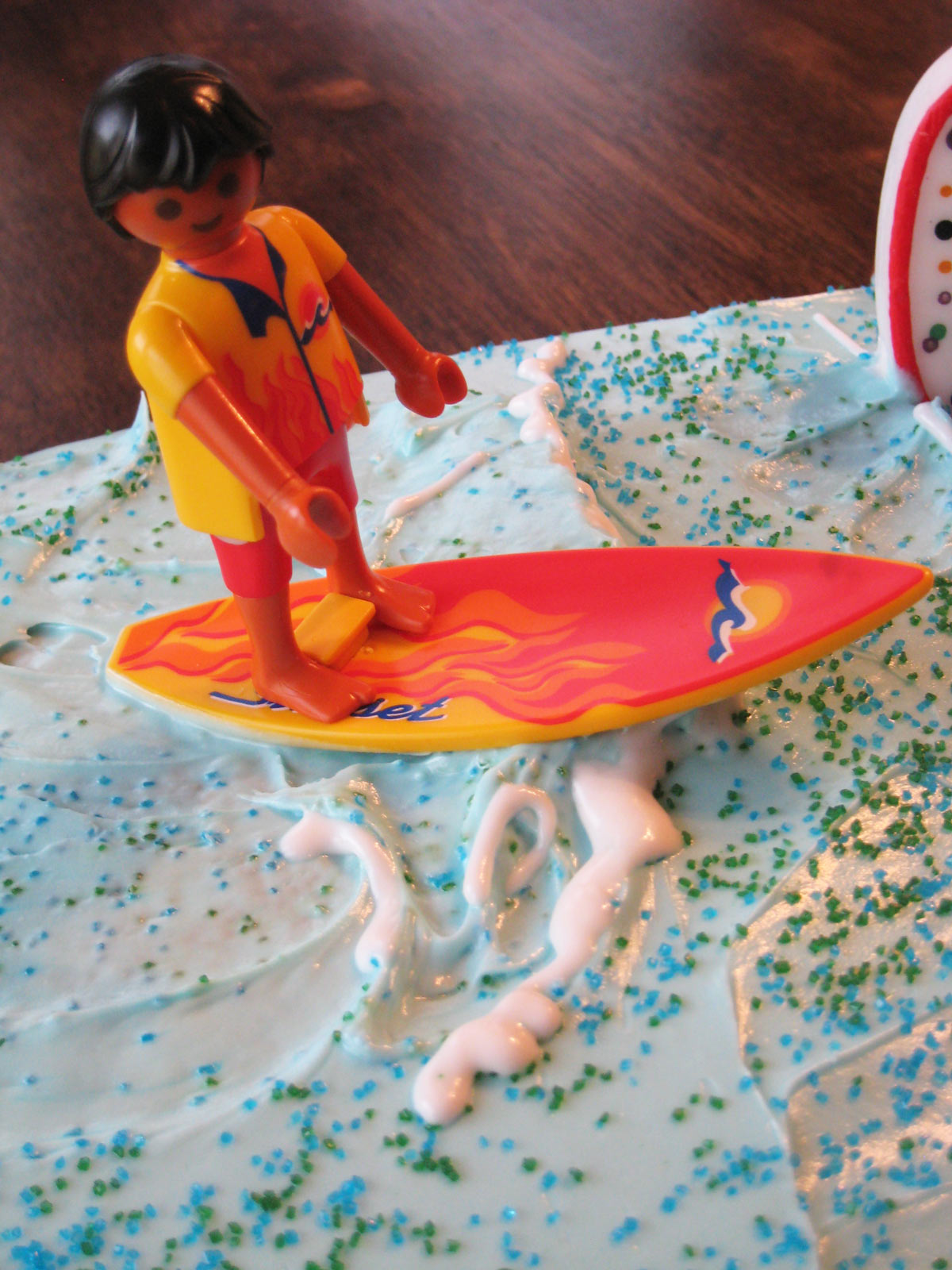 close up of toy surfer atop frosting wave on cake.