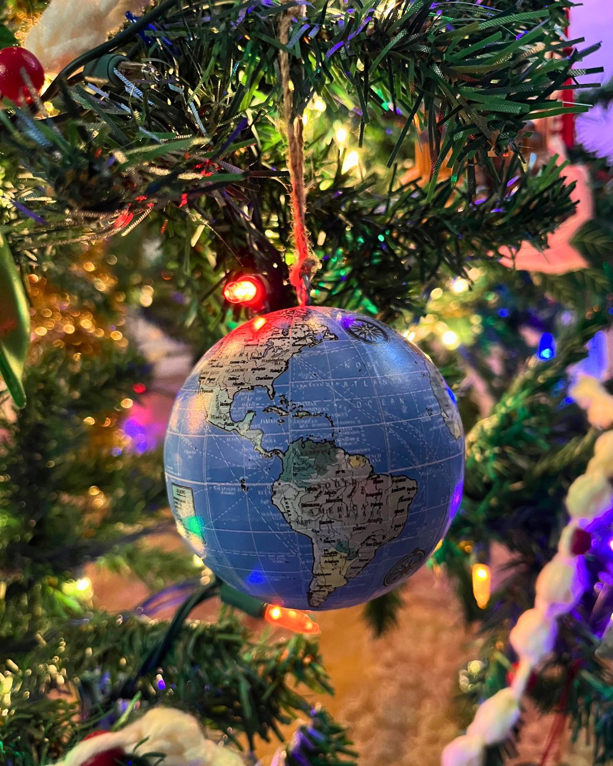 a globe ornament hanging from the christmas tree.
