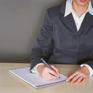 A woman sitting at a table with a pad and pen.