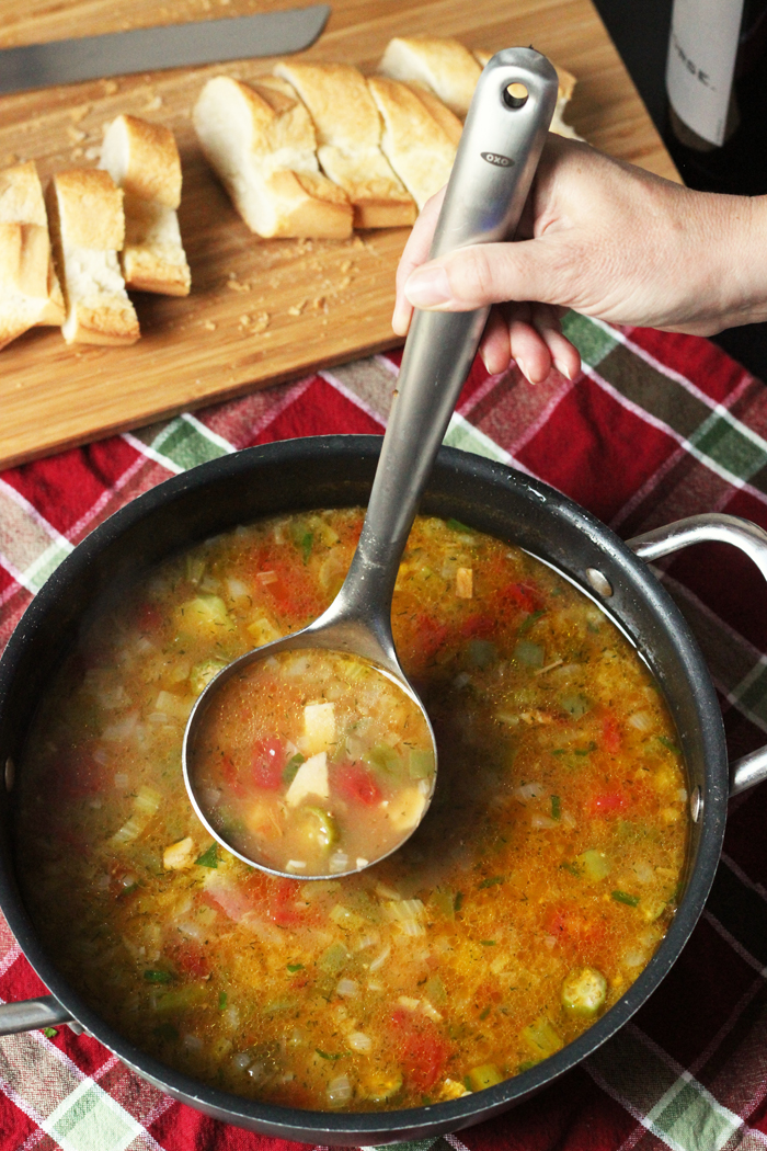 pot of chicken gumbo soup with a ladle and bread on the side