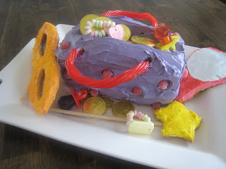 A cake decorated like a purple purse with candy jewelry and chocolate coins. 