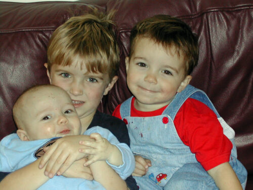 Three brothers on a couch, big brother holding the baby.