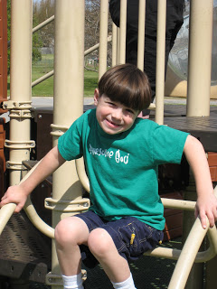 Boy in green shirt on playground equipment looking at the camera.