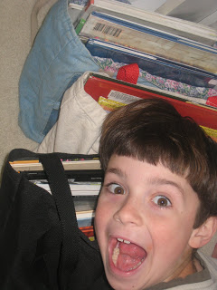 A little boy looking at the camera with excitement over bags of library books.