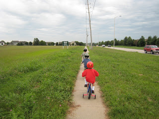 Line of boys riding bikes on a trail through the grass.