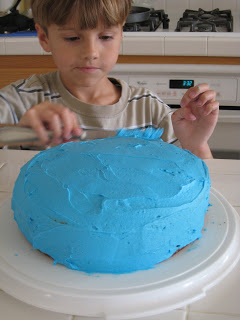 boy decorating layer cake with blue frosting.