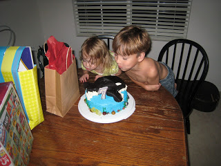 A little boy sitting at a table with a birthday cake, blowing out the candles.