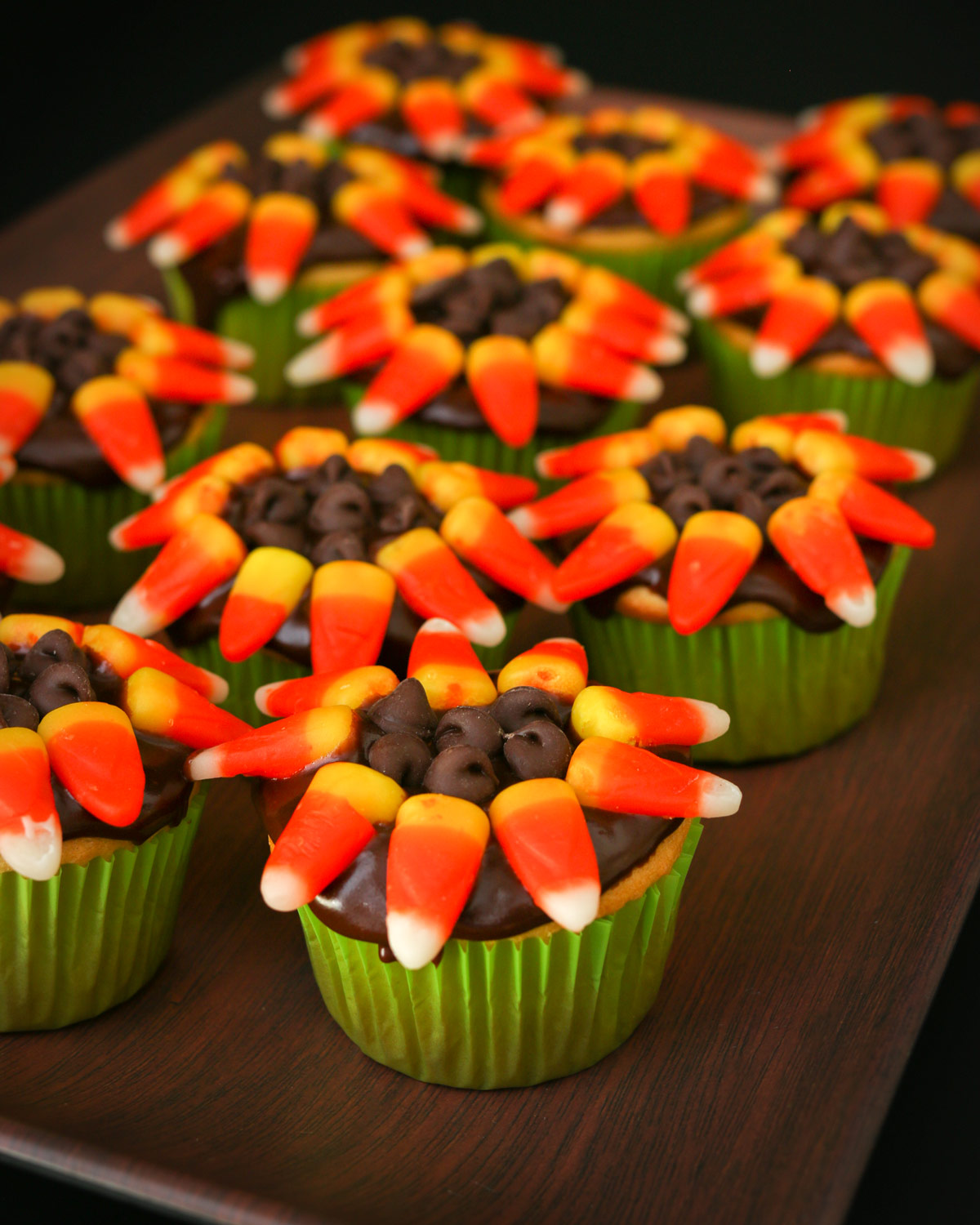 array of flower cupcakes on a brown tray from a side angle.