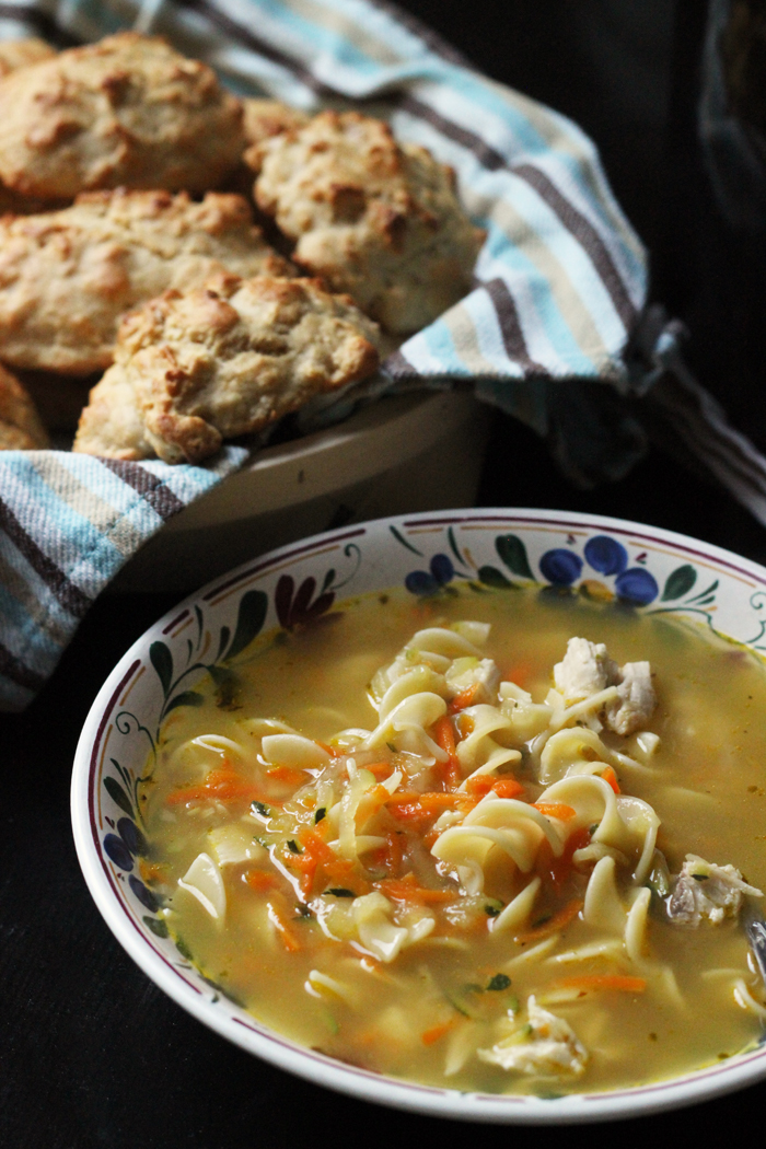 bowl of chicken noodle soup with a basket of biscuits
