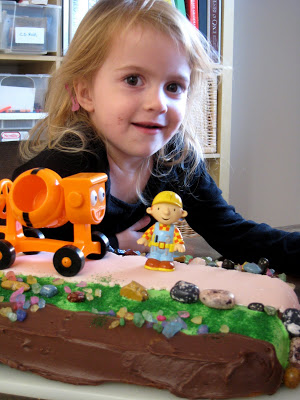 A little girl sitting at a table with a birthday cake topped with Bob the Builder.