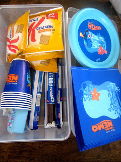Plastic box with nemo cups, plates, and napkins as well as snacks.