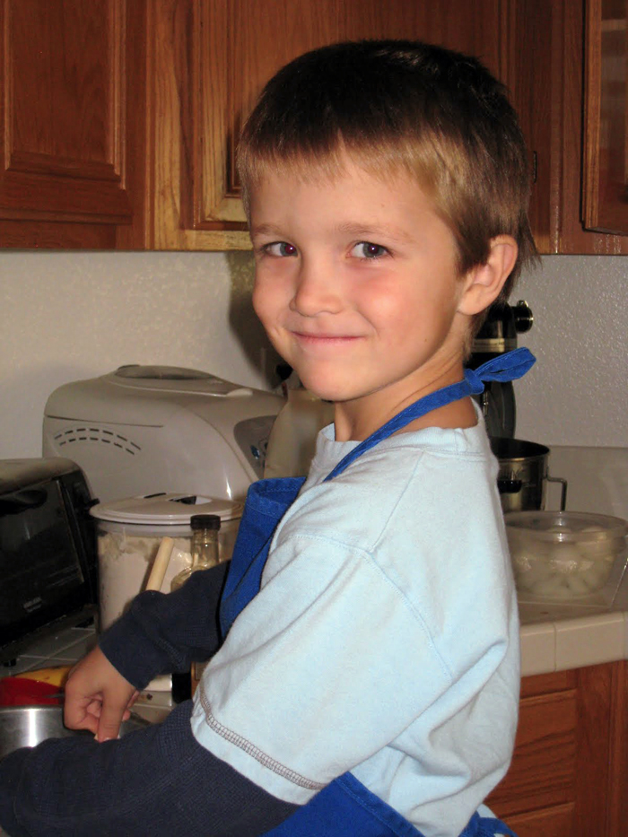 boy in blue apron cooking in kitchen