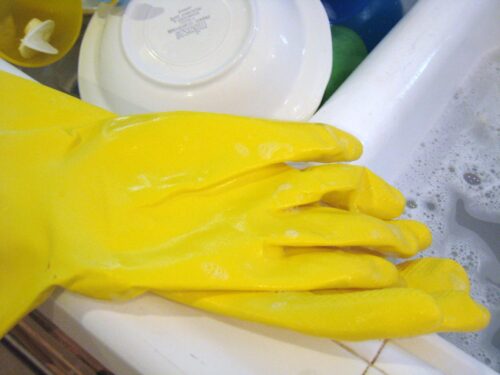 Dishwashing gloves on edge of sink full of soapy water and washed dishes.