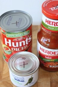 A close up of a salsa bottle and canned tomatoes with markings on the lids.