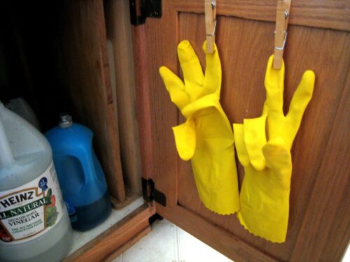 Yellow dishwashing gloves hanging on the inside of a cupboard.