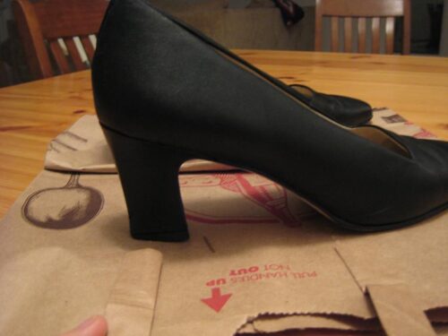 Black heels on paper grocery sack on kitchen table.