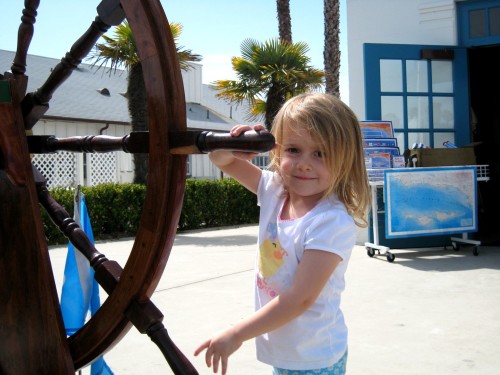 A little girl holding a ship\'s wheel at Maritime Museum in Santa Barbara.