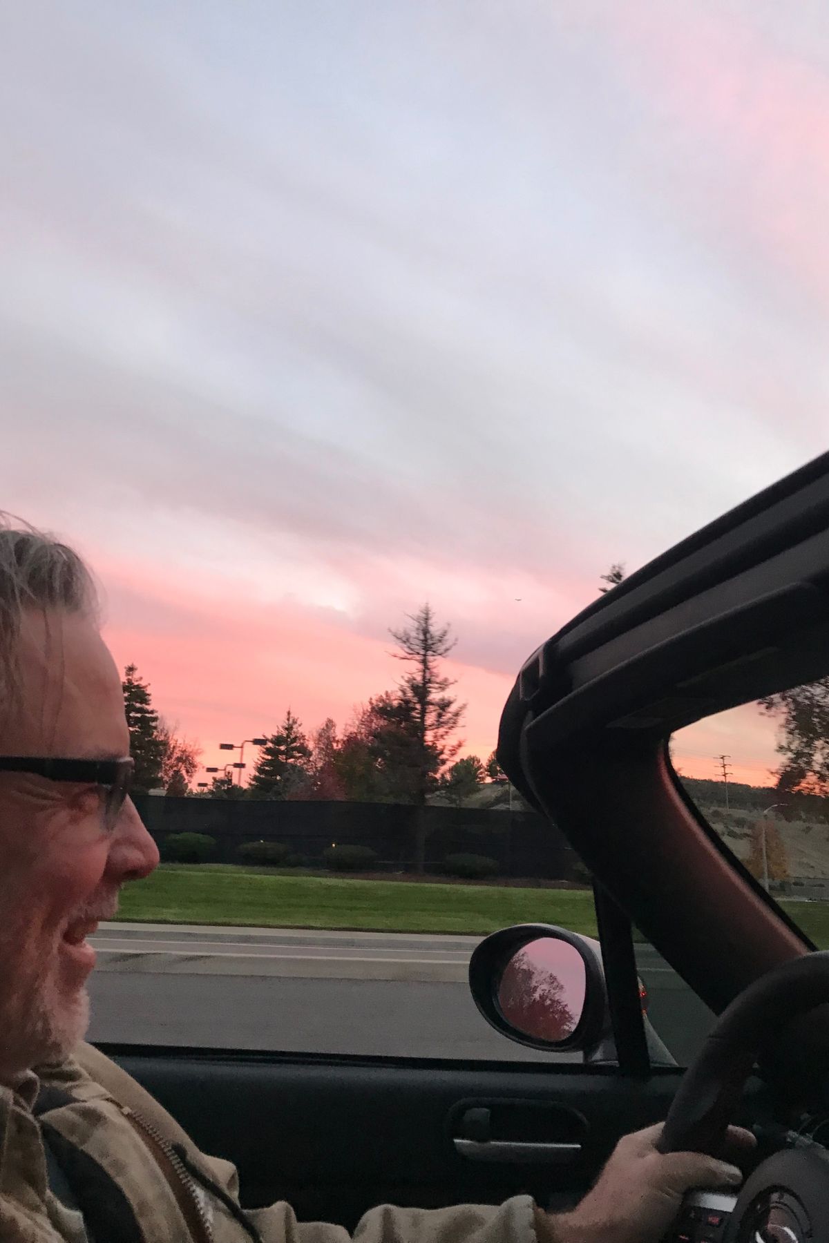 man driving a convertible at sunset.