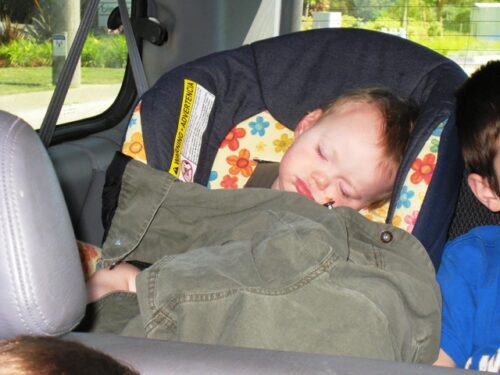 Baby sleeping in car seat, covered with a sibling's coat.