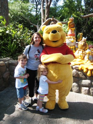 Mom and kids standing next to a Winnie the Pooh character at Disneyland.