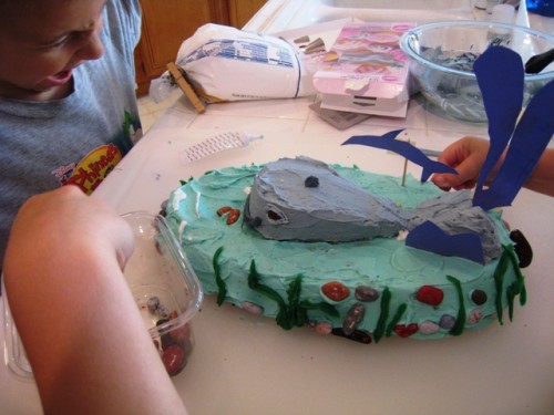 Decorating a whale birthday cake with candy rocks.