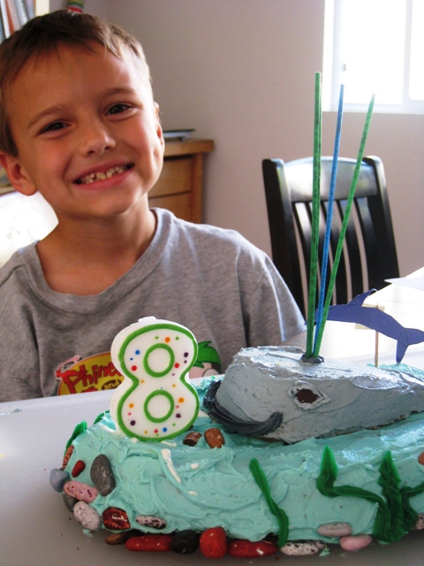 A little boy sitting at a table with a whale birthday cake with an 8 calendar.