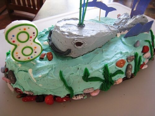 A whale birthday cake with an 8 candle on a table.