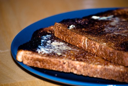 A plate with pieces of burnt and buttered toast.