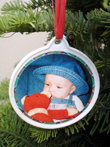 A Christmas ornament with a picture of a baby and a red teddy bear.