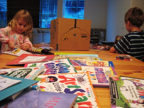 A little girl sitting at a table in front of a stack of craft books.