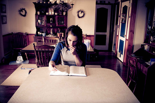 A person sitting at a table in a room reading the Bible.