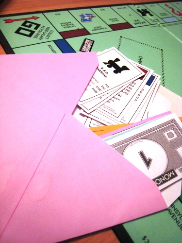 Monopoly money and cards on board in a pink envelope.