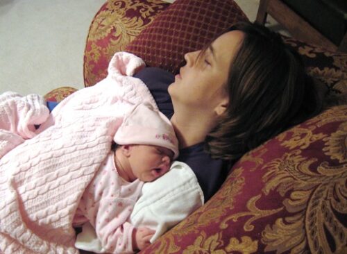 A mom asleep on the couch with a newborn sleeping on her chest.