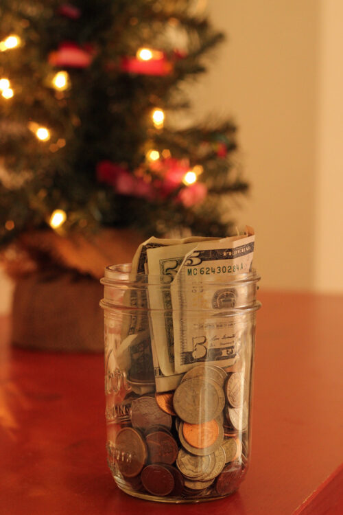jar of money in front of lit table top Christmas tree.
