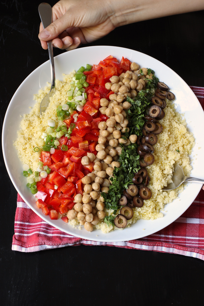 large white bowl of couscous with onions, peppers, beans, cilantro, and olives