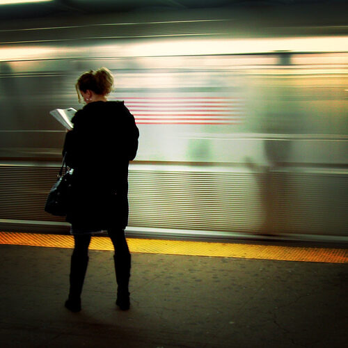 A person standing on a subway platform with light blur in background.
