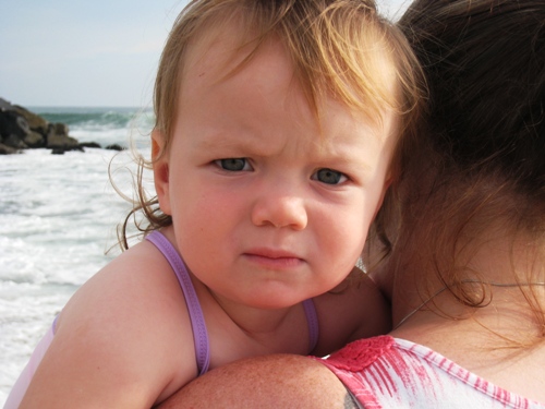 A little girl hugging mom and looking at the camera over her shoulder.