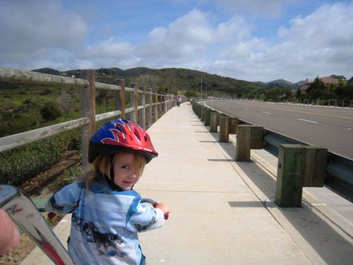 Girl wearing helmet, riding a bike and looking back at camera.