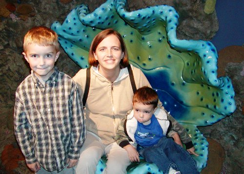 Mom and boys sitting in fake clam shell at Aquarium.