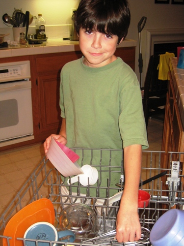 A boy standing in the kitchen unloading the dishwasher.