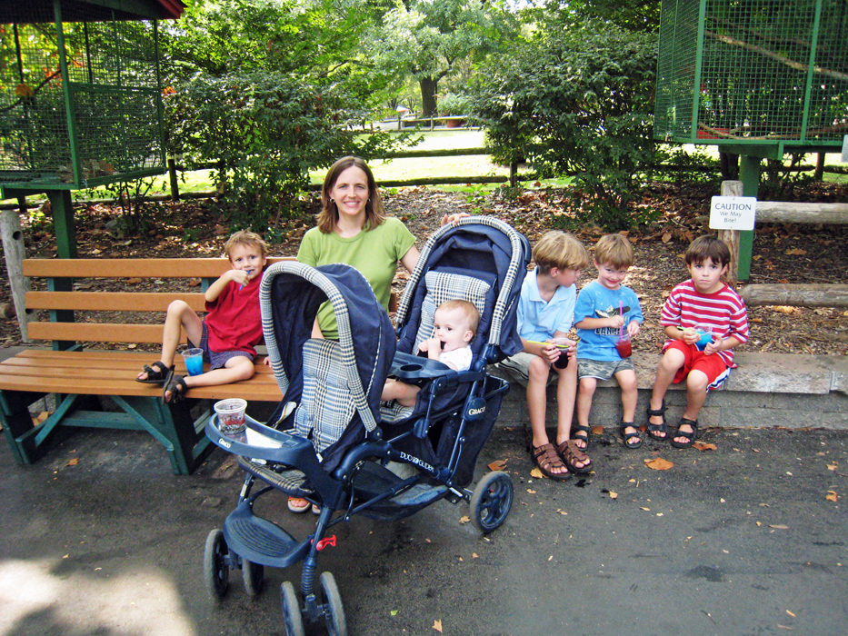 Mom and kids on bench with a stroller and baby in front of them.