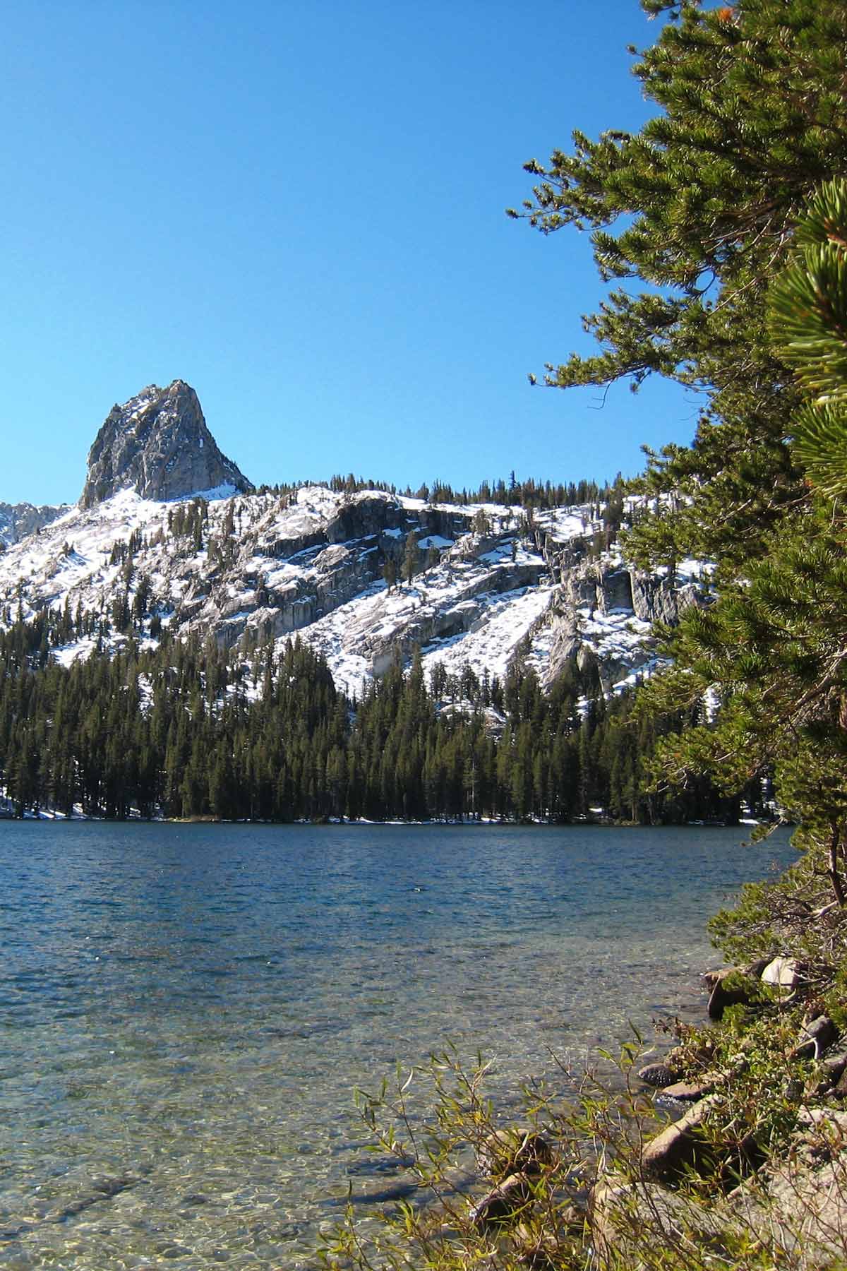 mountain lake with snow on the hill behind and fir trees.