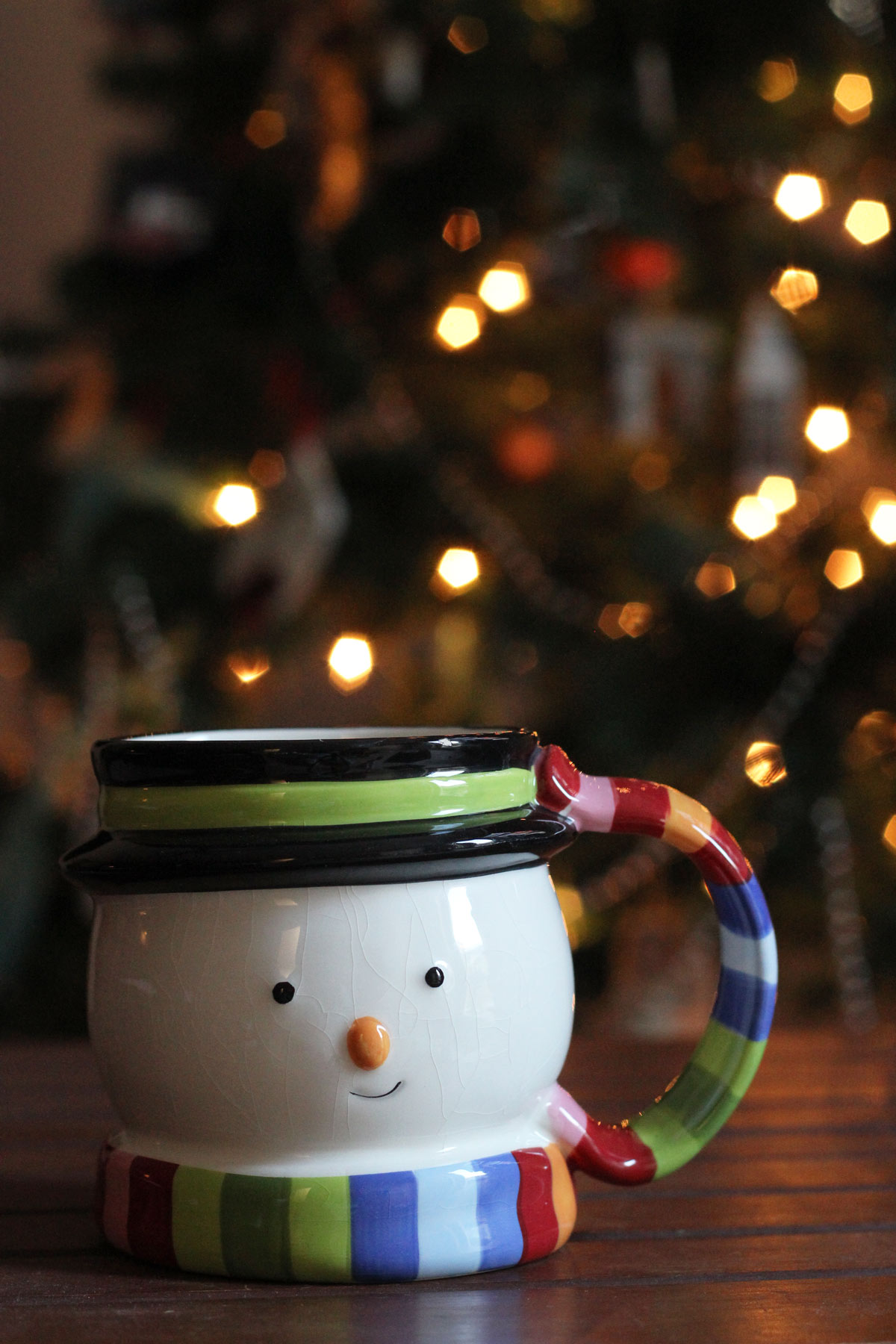snowman mug on table in front of lit christmas tree.