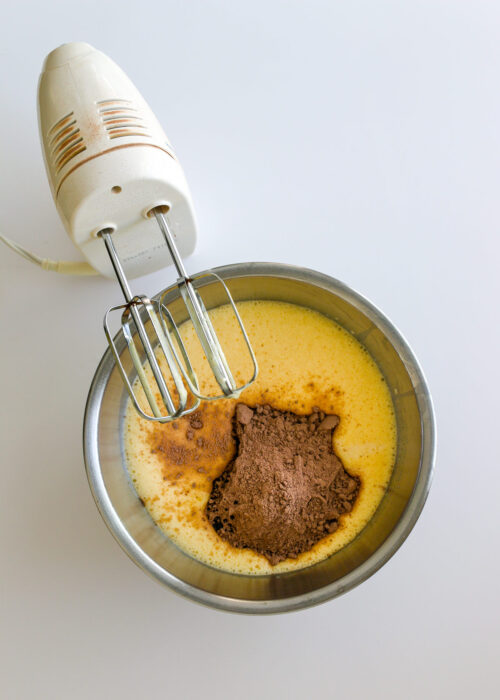 hand mixer with beaters and bowl with eggs and chocolate powder added.