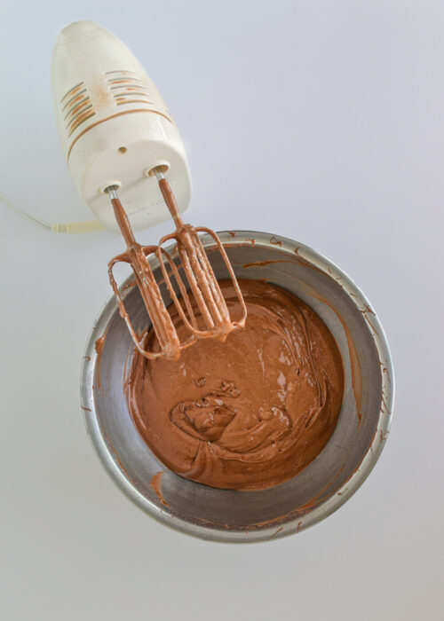 cake batter in bowl next to mixer with chocolate on the beaters.