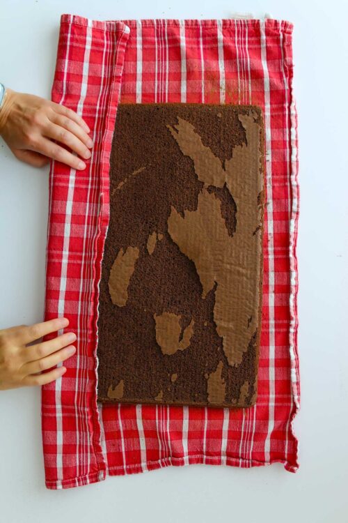 hands folding towel edge over cake to start rolling.